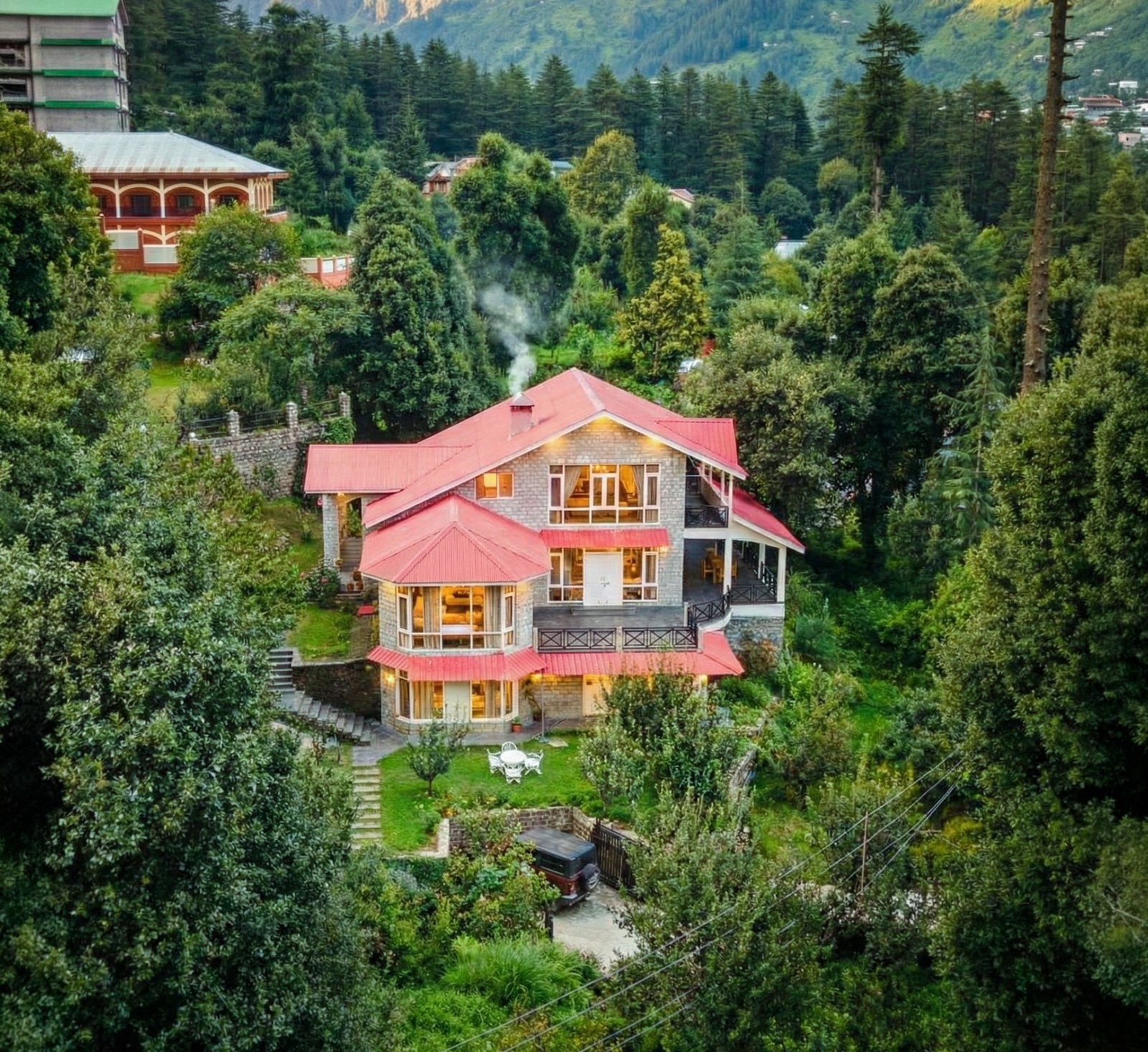 Forestbound Cottage — wide aerial view of the luxury villa and garden surrounded by towering cedar and pine forests in Manali, Himachal Pradesh with snow-capped Himalayan peaks in the background
